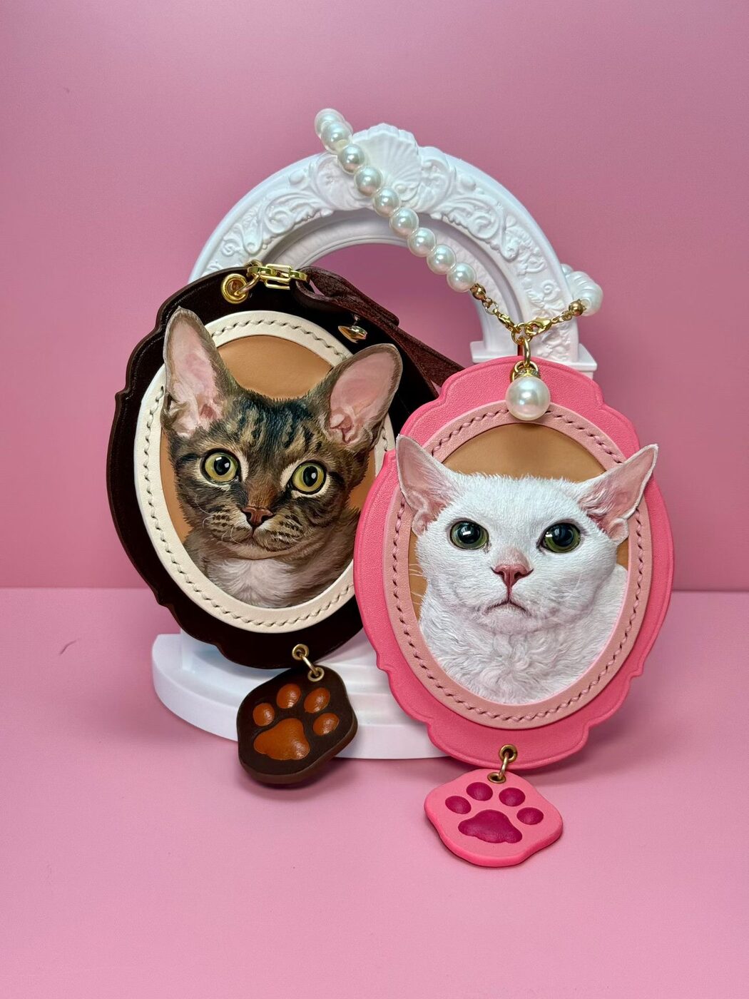 Two custom leather cat portraits displayed on a pink background